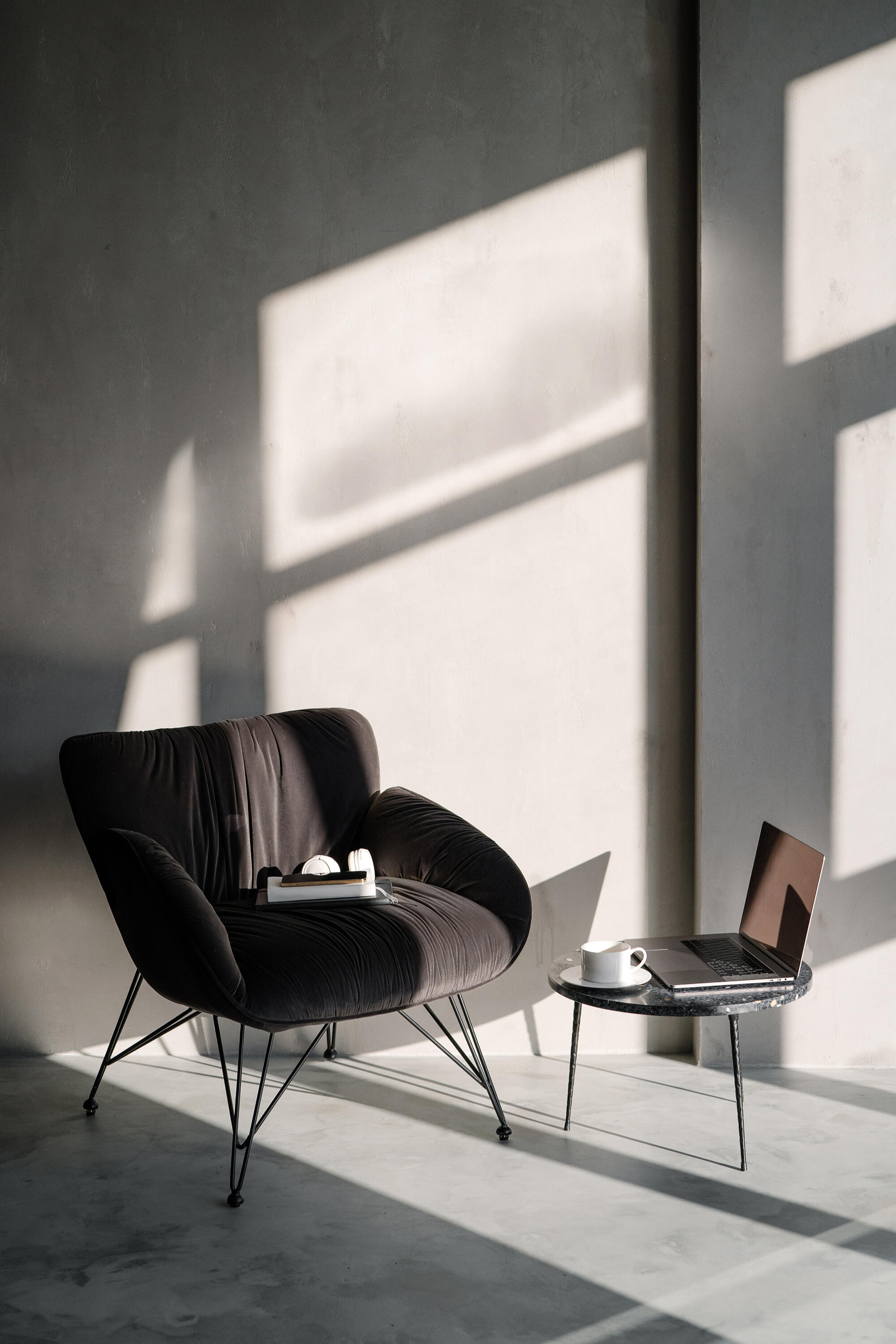 Black lounge chair beside a laptop in a minimalist sunlit workspace.